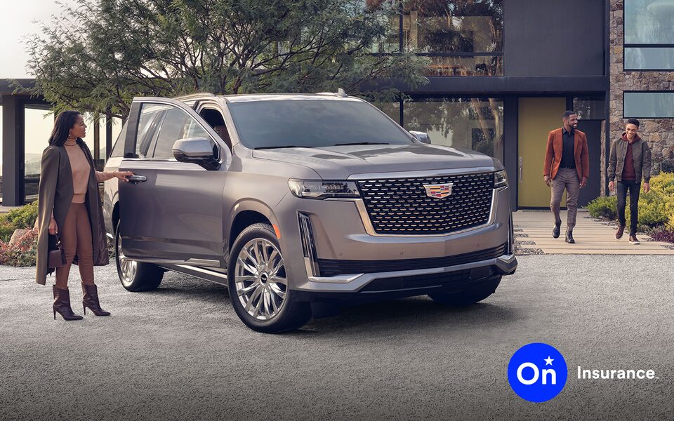 Cadillac Escalade sits in the driveway of a modern home. A woman stands at the open passenger side door while a man and a young boy walk out of the home toward the car. OnStar Insurance logo is in the bottom right corner.