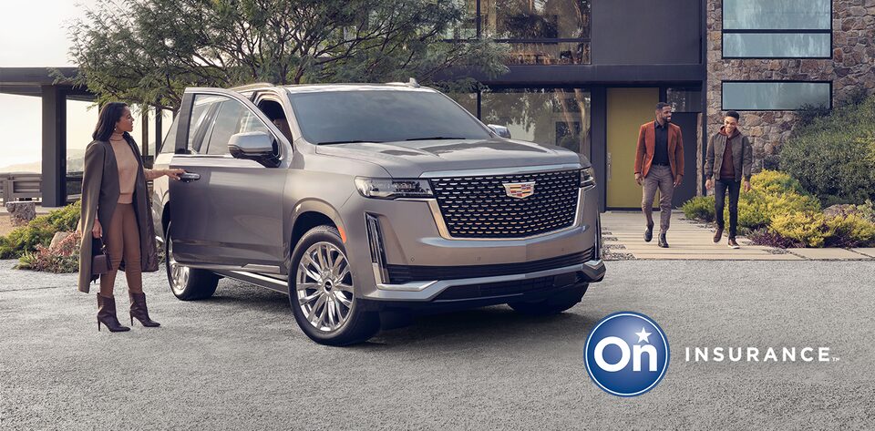 Cadillac Escalade sits in the driveway of a modern home. A woman stands at the open passenger side door while a man and a young boy walk out of the home toward the car. OnStar Insurance logo is in the bottom right corner.