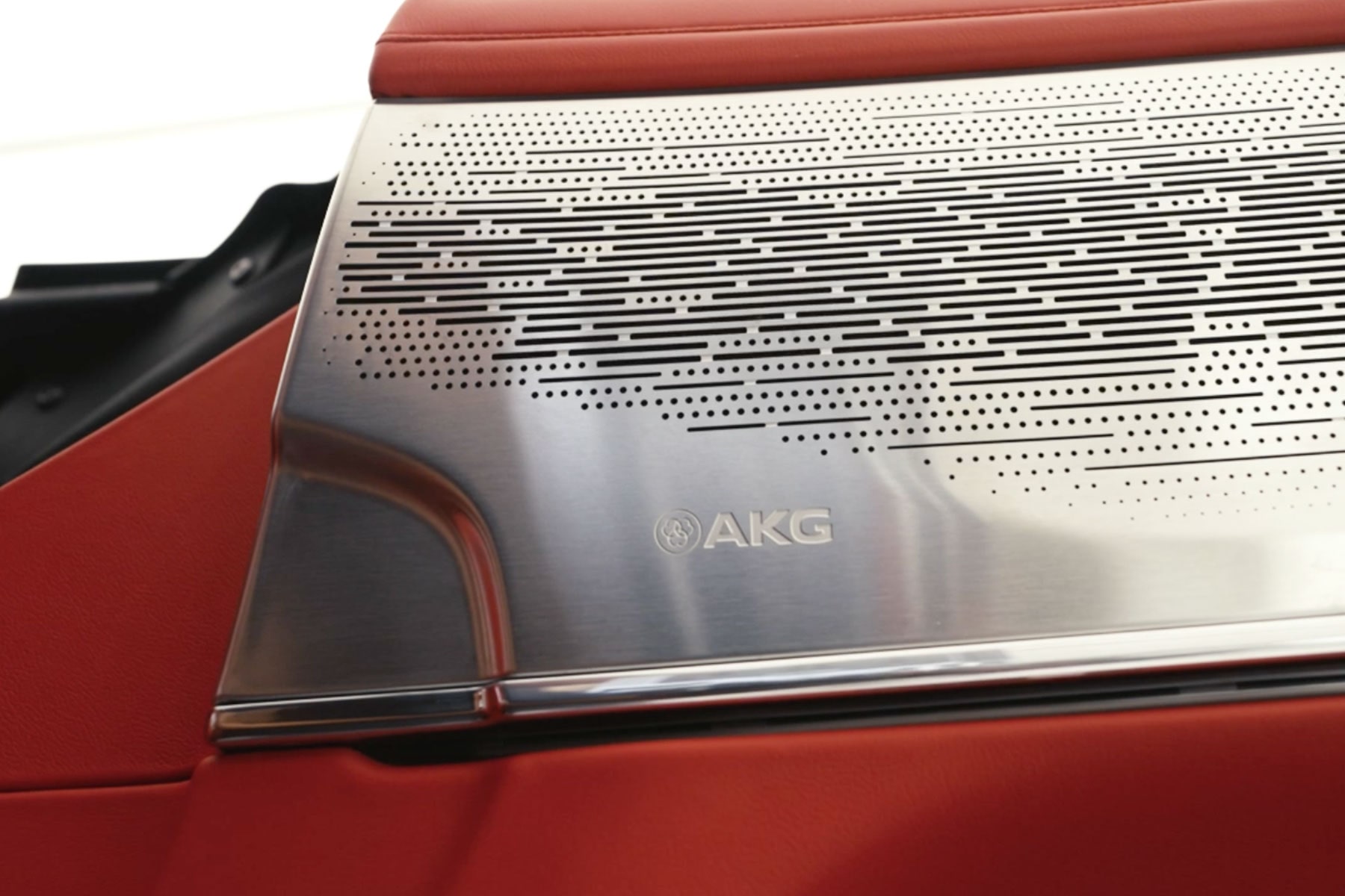 A Detailed View of an AKG Speaker Grille with a Brushed Metal Finish on a Red Cadillac Interior Door Panel