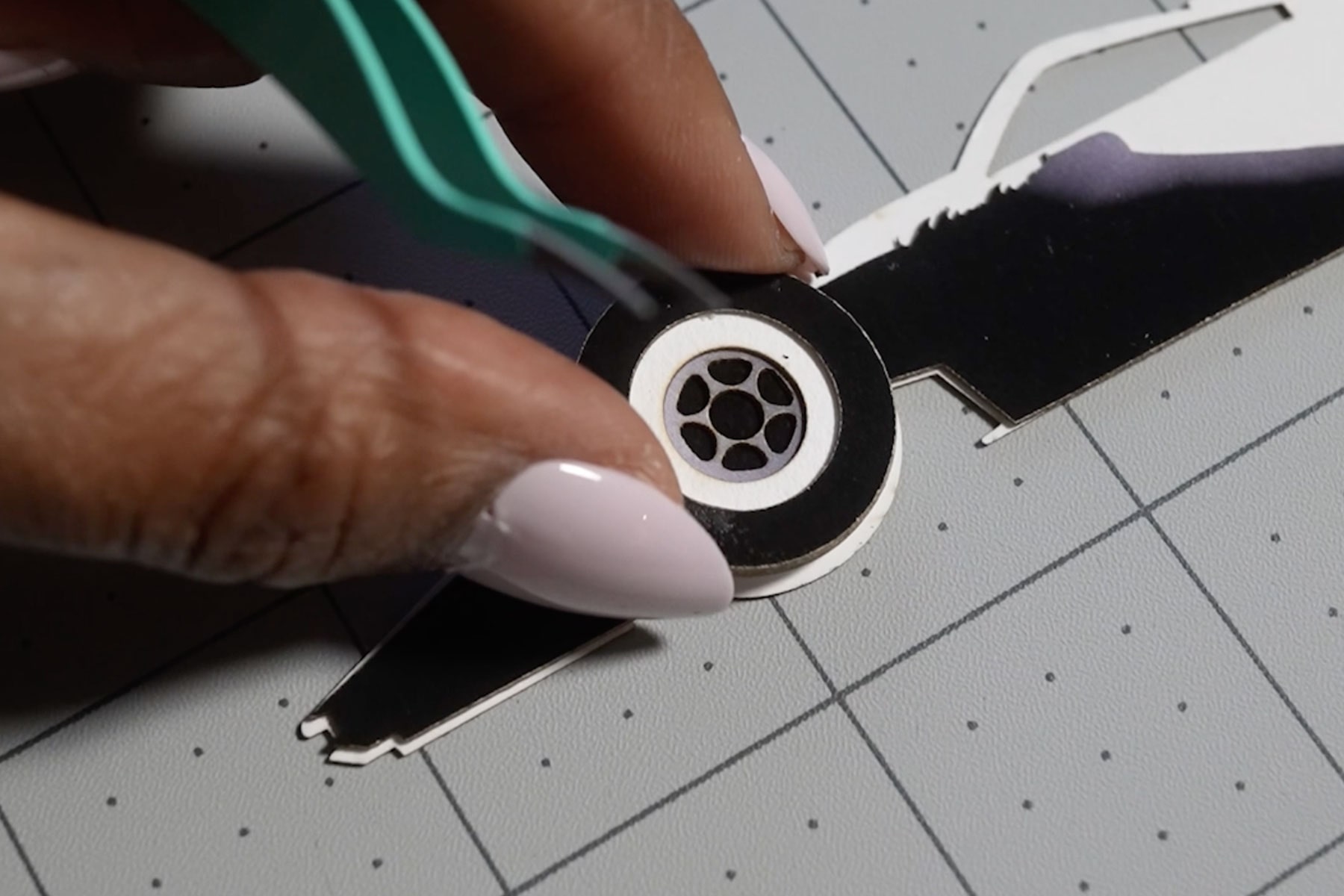 A Close-Up of Hands Using Tweezers to Assemble a Cadillac-Inspired Vehicle Artwork Cutout on a Precision Cutting Mat Surface