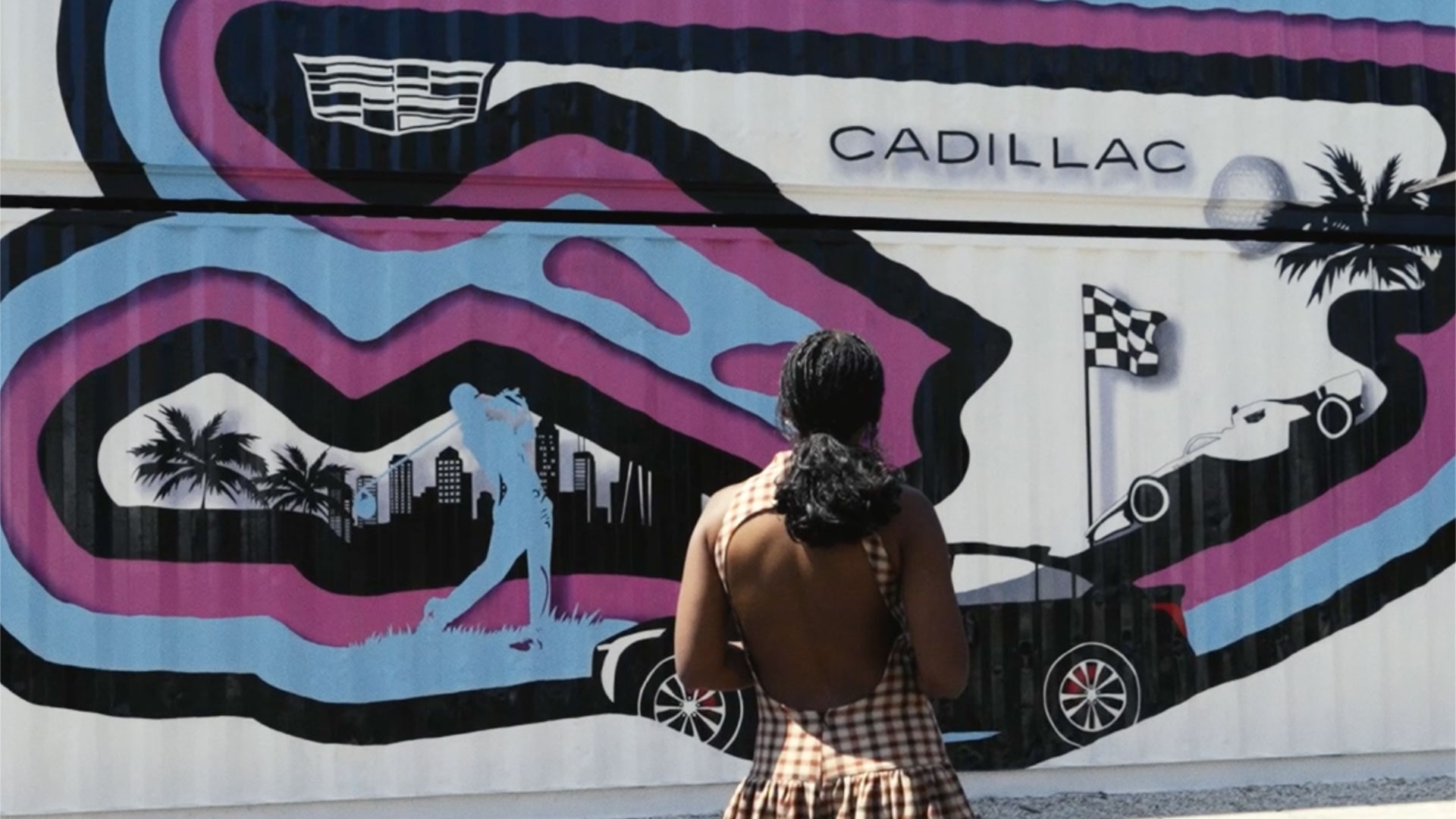 Melissa Koby Standing in Front of a Large Cadillac-Branded Mural Featuring a Cityscape and Racing-Inspired Artwork in Vibrant Pink, Blue, Black, and White Colors