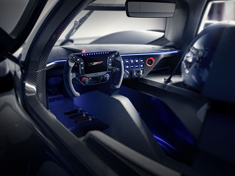 The Silver Cadillac V-ONE Concept Vehicle Driving at Speed in a Dark Tunnel Environment With Illuminated Headlights, Vertical LED Taillights, and a Prominent Rear Wing Accentuated by Motion Blur.