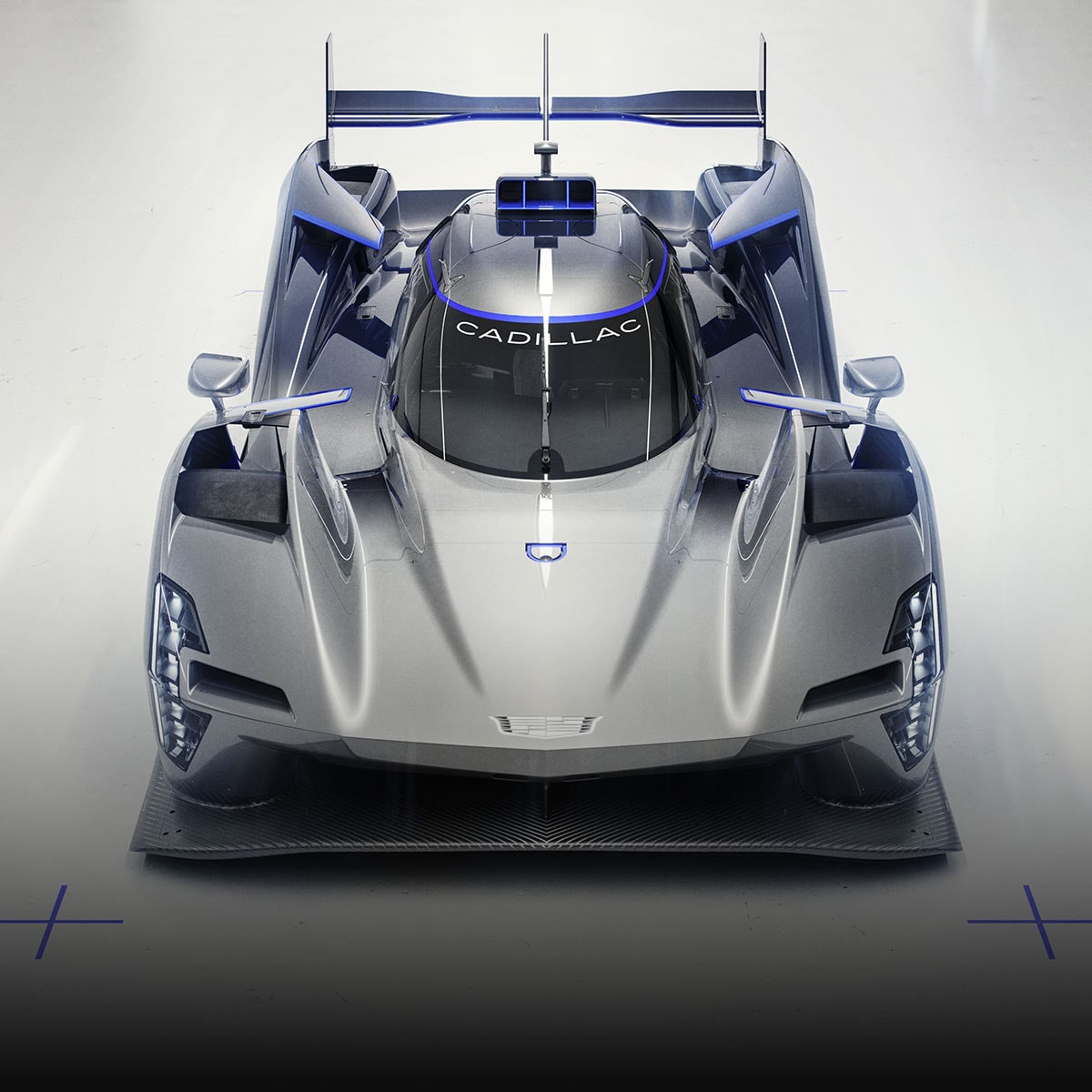 The Silver Cadillac V-ONE Concept Vehicle Positioned at a Front Three-Quarter Angle on a White Studio Floor With Blue Alignment Markers and an Oversized Rear Wing.