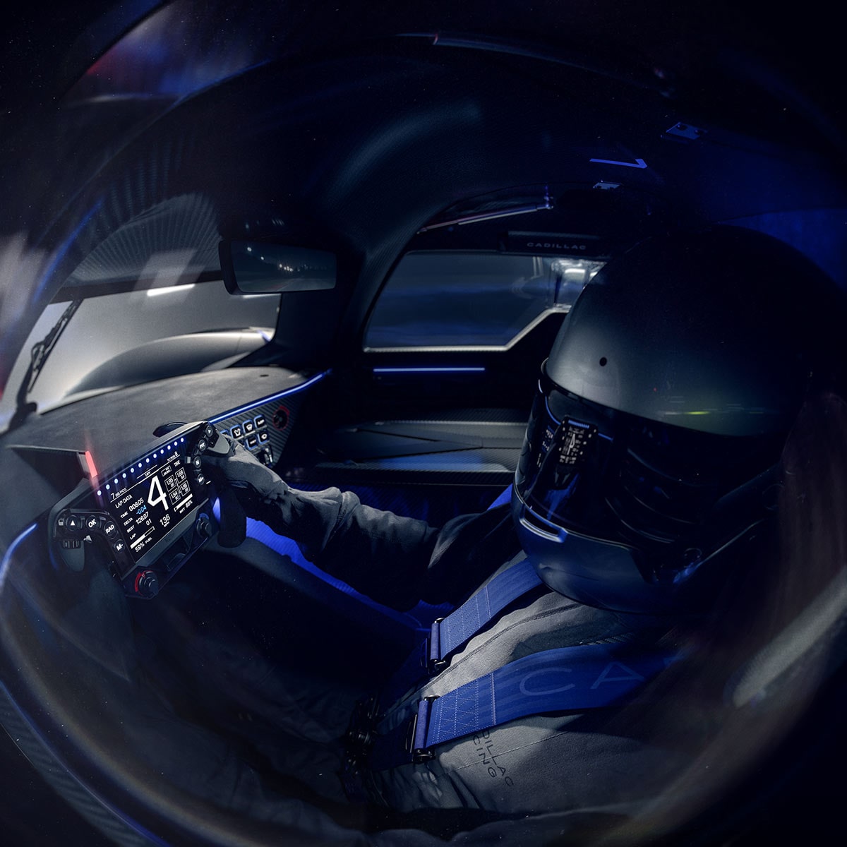 A View Into the Cockpit of the Silver Cadillac V-ONE Concept Vehicle Showing a Sculpted Racing Seat, Cadillac-Branded Blue Harness Straps, a Racing Helmet, a Digital Steering Wheel, and an Enclosed Carbon Fiber Interior Illuminated by Blue Ambient Lighting.