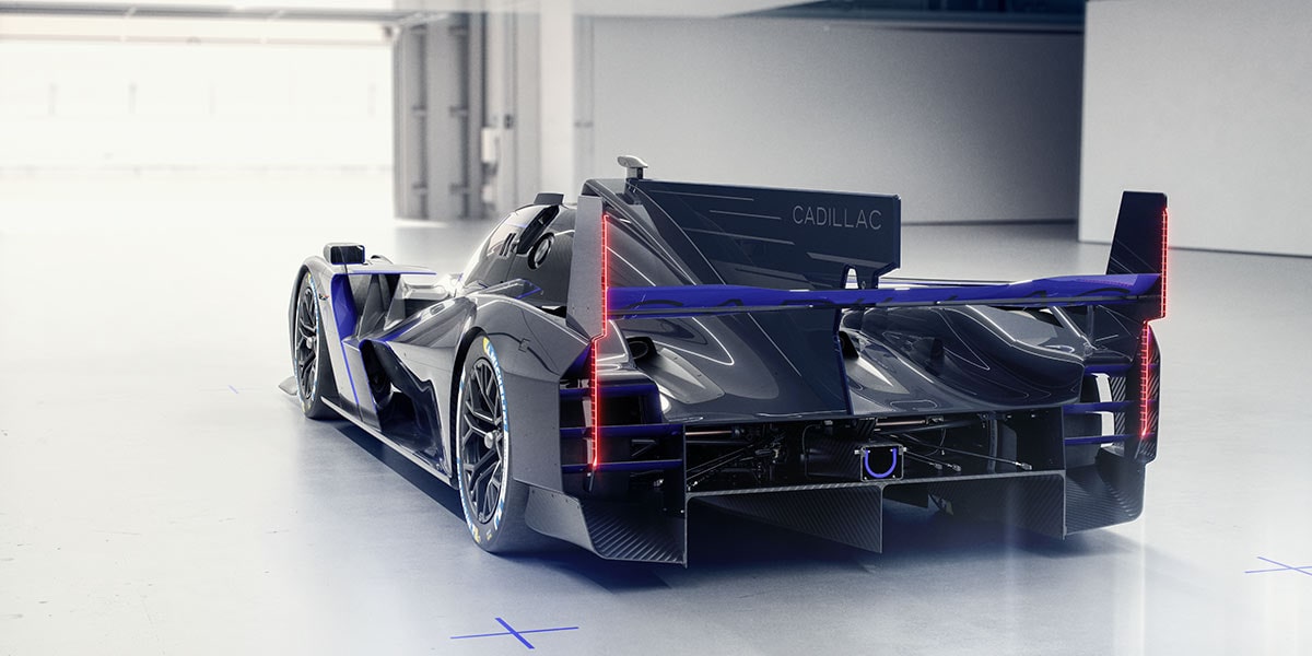 A Close-Up View of the Rear Section of the Silver Cadillac V-ONE Concept Vehicle Highlighting a Blue Carbon Fiber Rear Wing, Aerodynamic Fins, and a Vertical Red LED Taillight Integrated Into the Rear Bodywork.