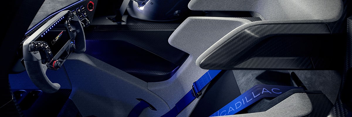 A Rear Three-Quarter View of the Silver Cadillac V-ONE Concept Vehicle Displaying a Large Rear Wing, Vertical LED Taillights, Aerodynamic Diffuser Elements, and Carbon Fiber Bodywork Inside a Bright White Studio.