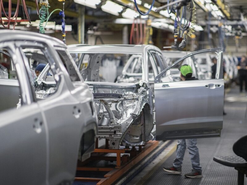 Man holding a door putting it on a vehicle on an assembly line