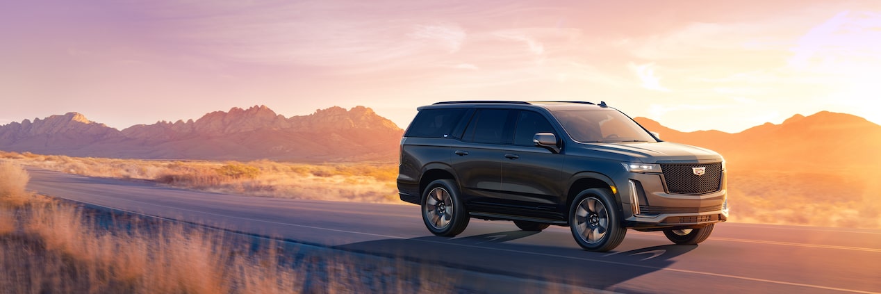2024 Cadillac Escalade Driving Down the Road with a Mountain Backdrop at Sunset