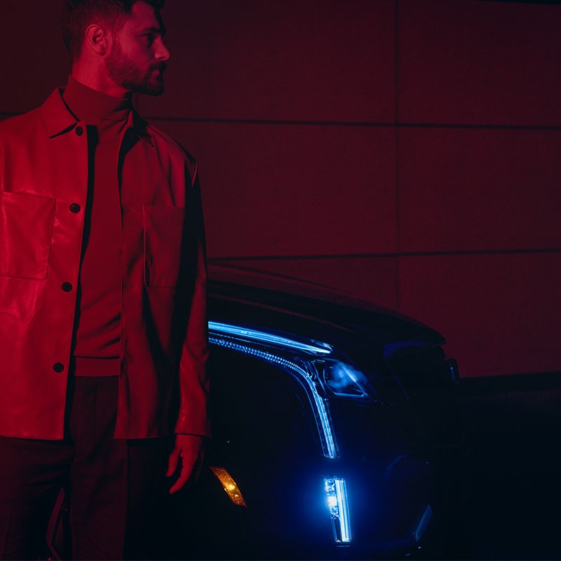 A Man Stands Next to His Cadillac XT5 at Night With Headlamps On