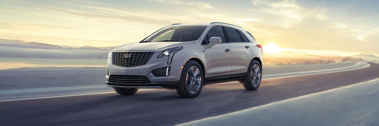 The 2024 Cadillac XT5 Driving on a Winding Road with Sun Rising in Background