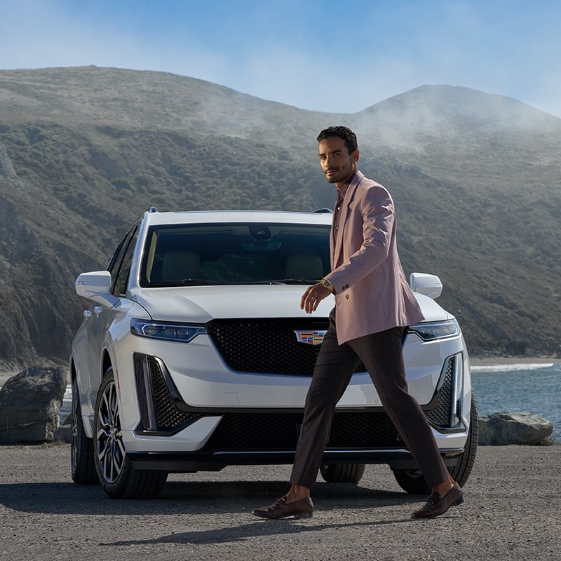 A Man Staring at the Camera Walks In Front of the Cadillac XT6 with a Stunning View in the Distance