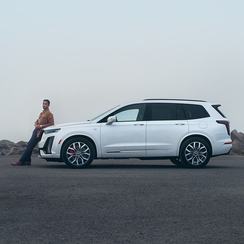 A Sharply Dressed Man Leans on the Hood of His Cadillac XT6