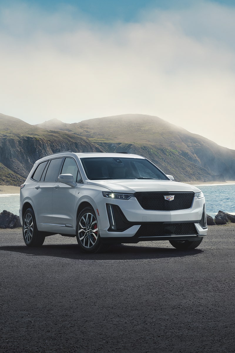 A Cadillac XT6 Parked Along the Coast with a View of a Mountain in the Distance