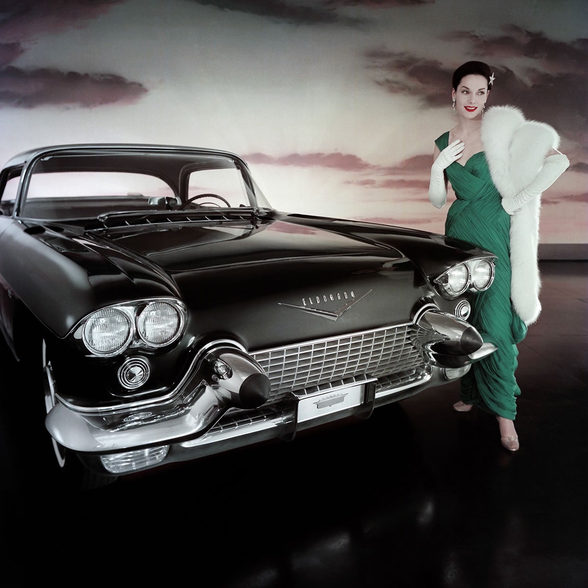 Una mujer con vestido glamoroso y abrigo de piel posa junto a un Cadillac Eldorado