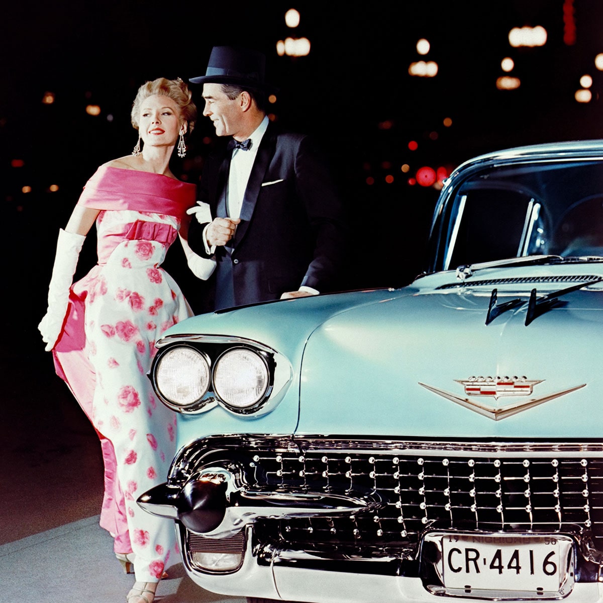 Una pareja elegante posa delante de un vehículo Cadillac clásico