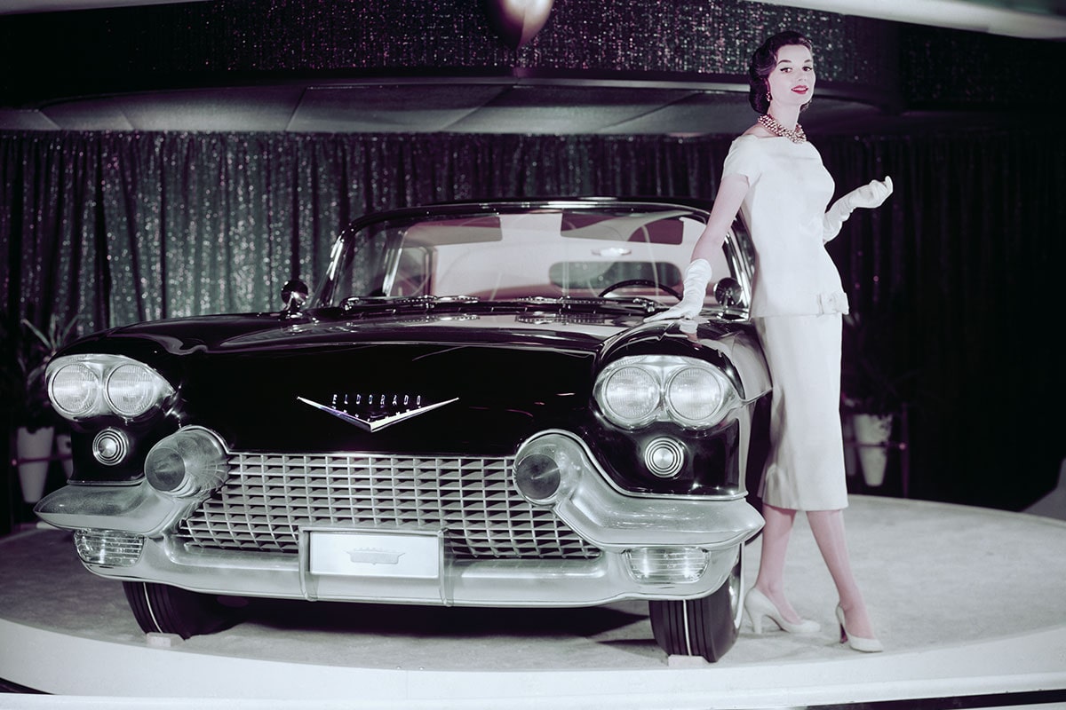 Una mujer posa junto a un Cadillac Eldorado en una plataforma giratoria para autos