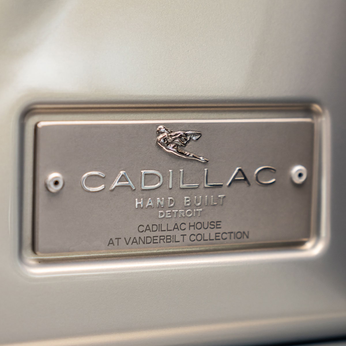 A Close-Up of the Cadillac Plaque With Text 'Cadillac Hand Built Detroit Cadillac House at Vanderbilt Collection'.