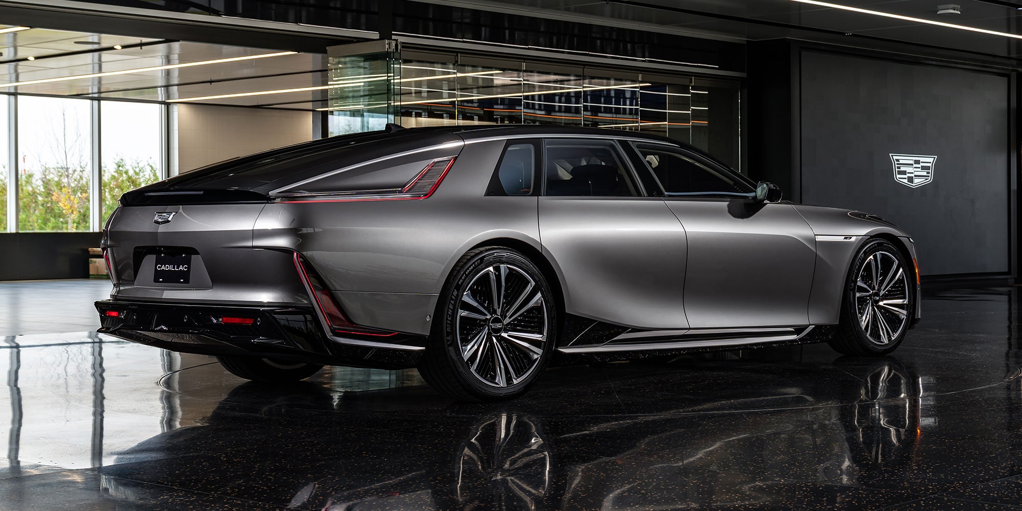 The Side Profile of the Dark Gray Cadillac CELESTIQ Parked on a Glossy Floor, with Be Iconic on the Wall in the Background.