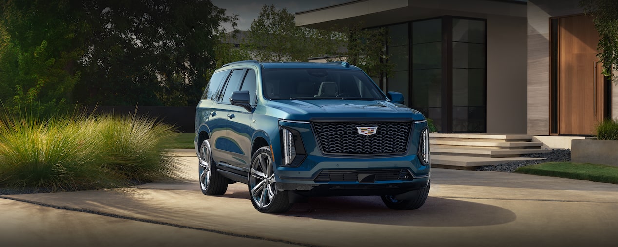 Three-quarter View of a Blue 2025 Cadillac Escalade Parked in Front of a Modern Home