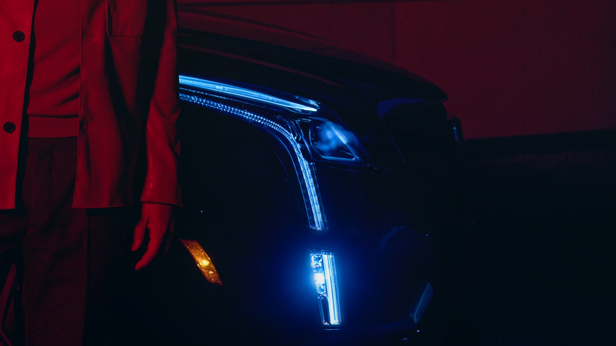 A Man Stands Next to His Cadillac XT5 at Night With Headlamps On