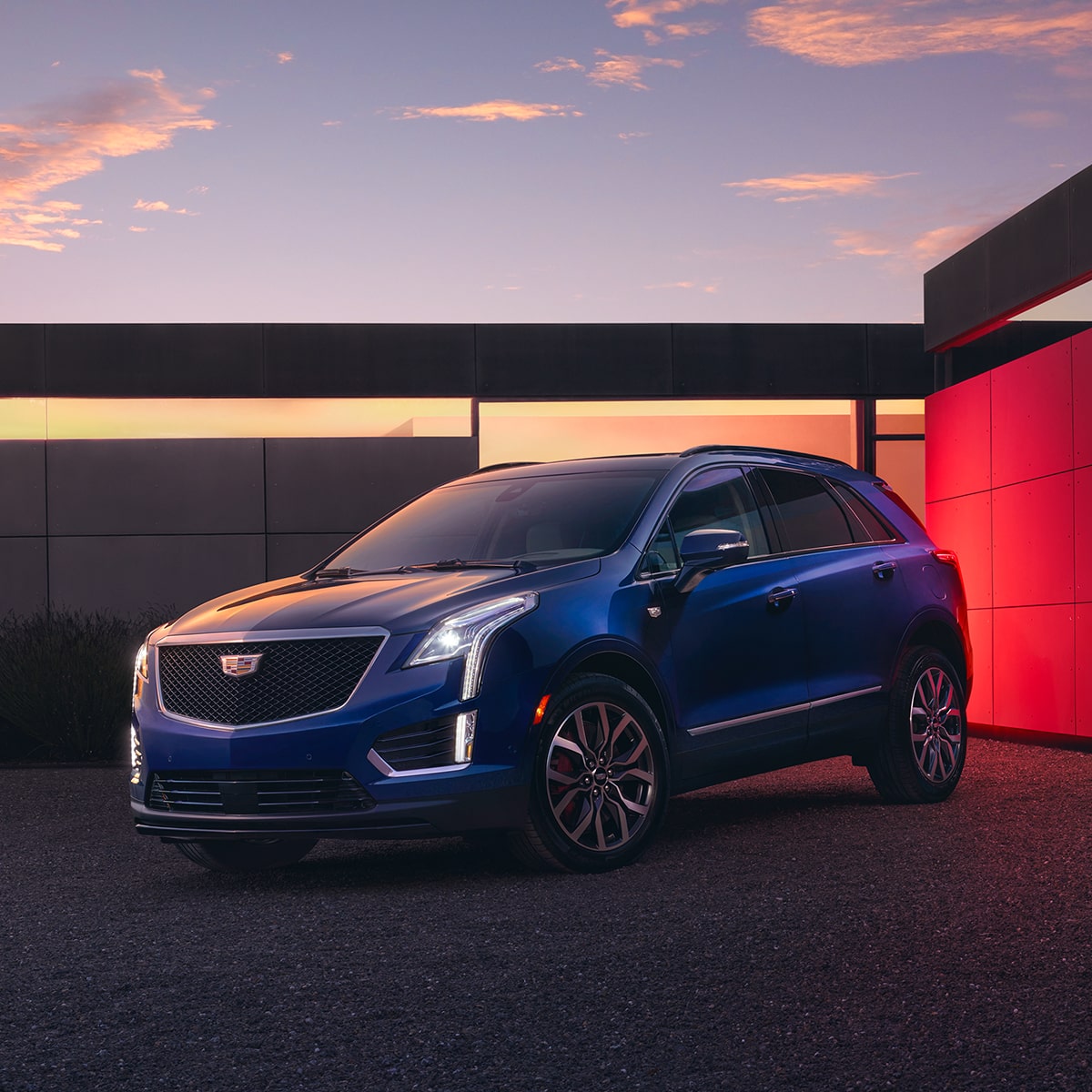 Una hermosa Cadillac XT5 2025 estacionada al anochecer frente a una casa moderna con las luces encendidas