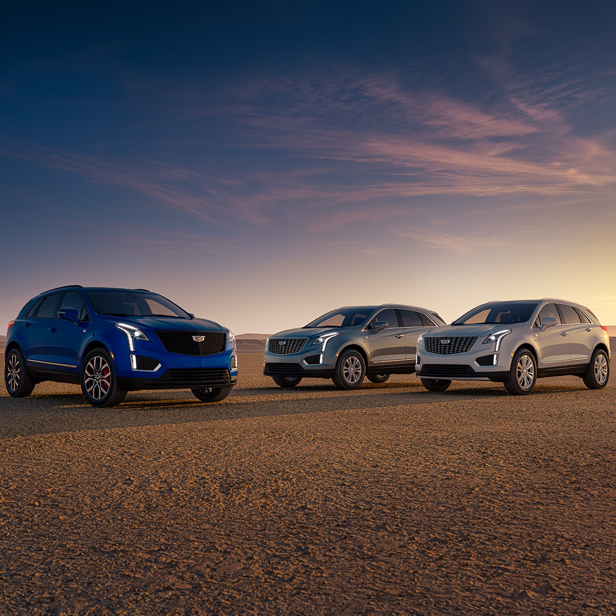 Tres vehículos Cadillac XT5 2025 estacionados en el desierto, durante el atardecer
