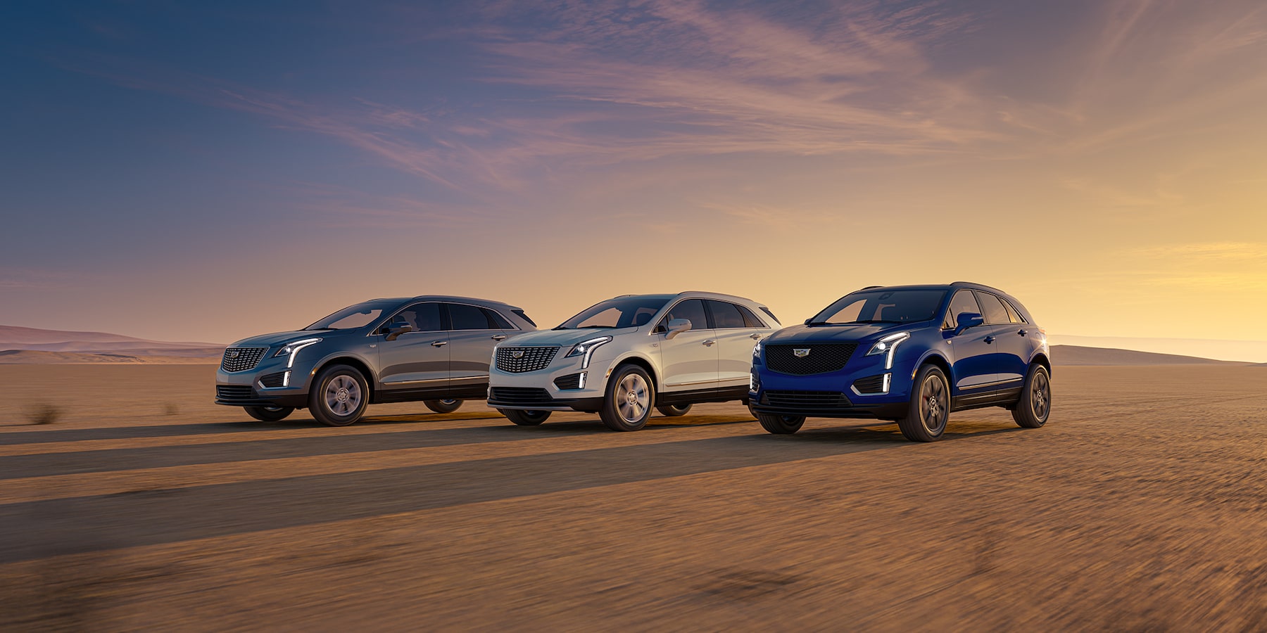 Grey, White and Blue 2025 Cadillac XT5 SUV's driving on desert terrain during sunset
