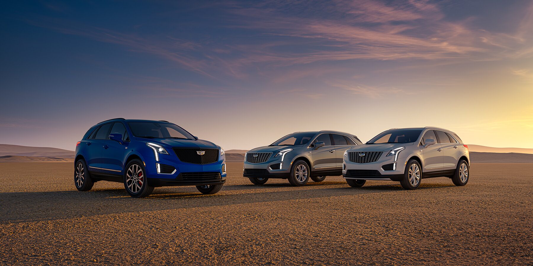 Blue, Silver, and white 2025 Luxury Compact Cadillac XT5 SUV's parked next to each other on sandy terrain
