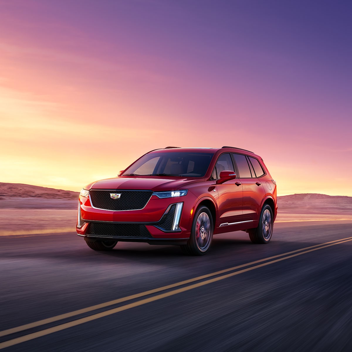 Vista de medio perfil de una Cadillac XT6 en Rojo circulando por un camino, con un atardecer de fondo