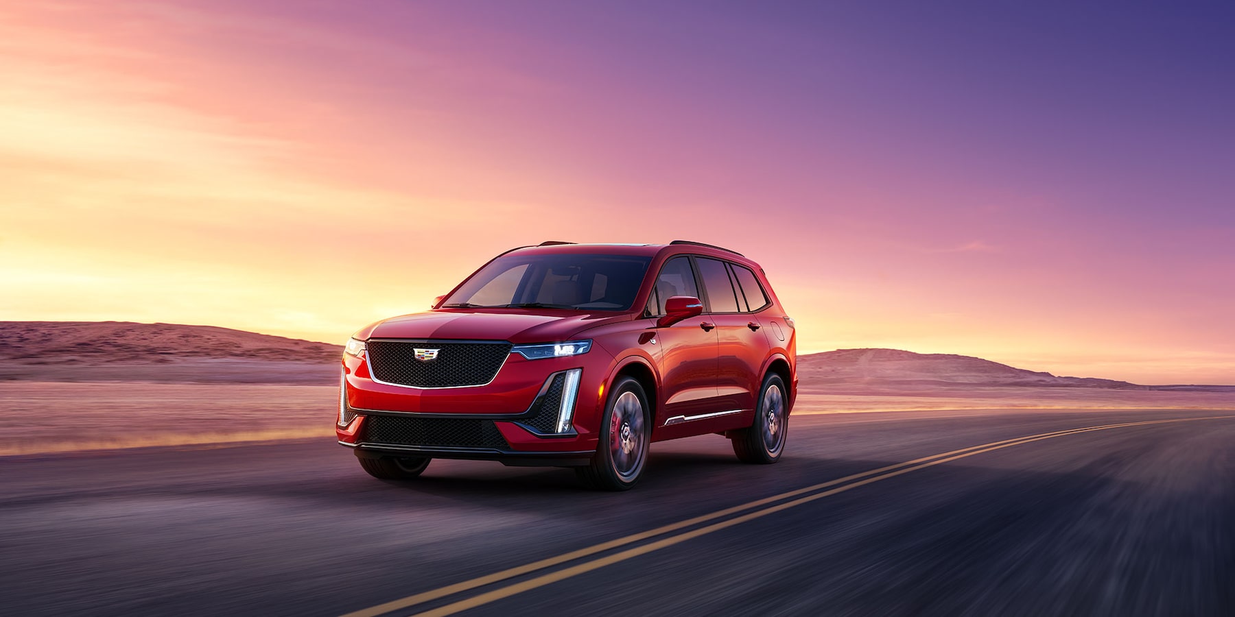 The Mid-sized 2025 Cadillac XT6 SUV with Red exterior on driving down a empty interstate during a sunset