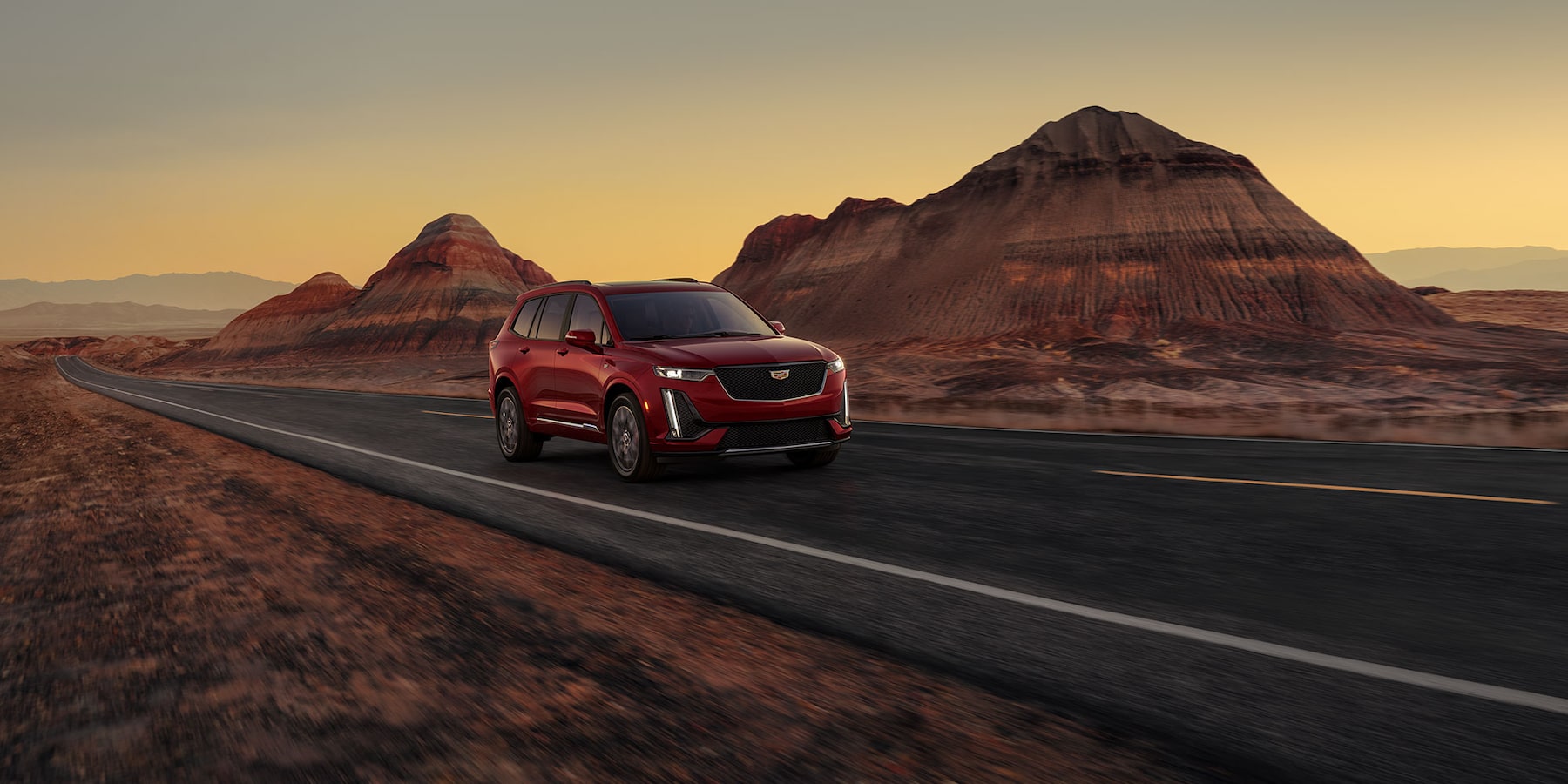 A Dark Red Cadillac XT6 3-Row Luxury SUV speeding down a empty two lane highway in a desert