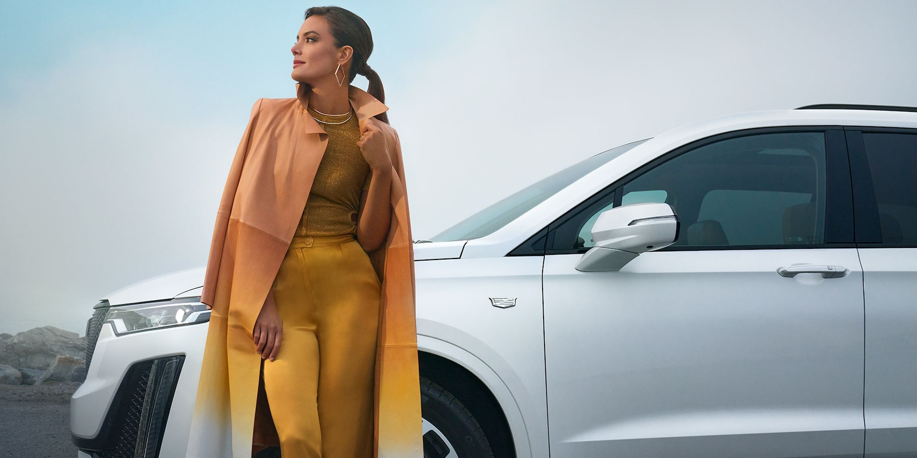 2025 Cadillac XT6 in white with fashionable woman leaning against the front fender