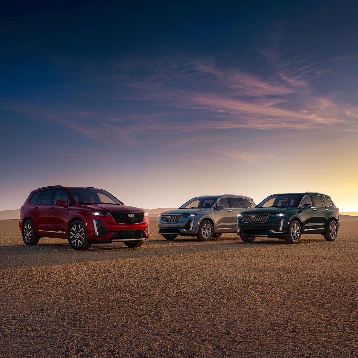 Vista de medio perfil de tres Cadillac XT6 en Rojo, Plata y Verde Oscuro orientadas hacia distintas direcciones en un desierto