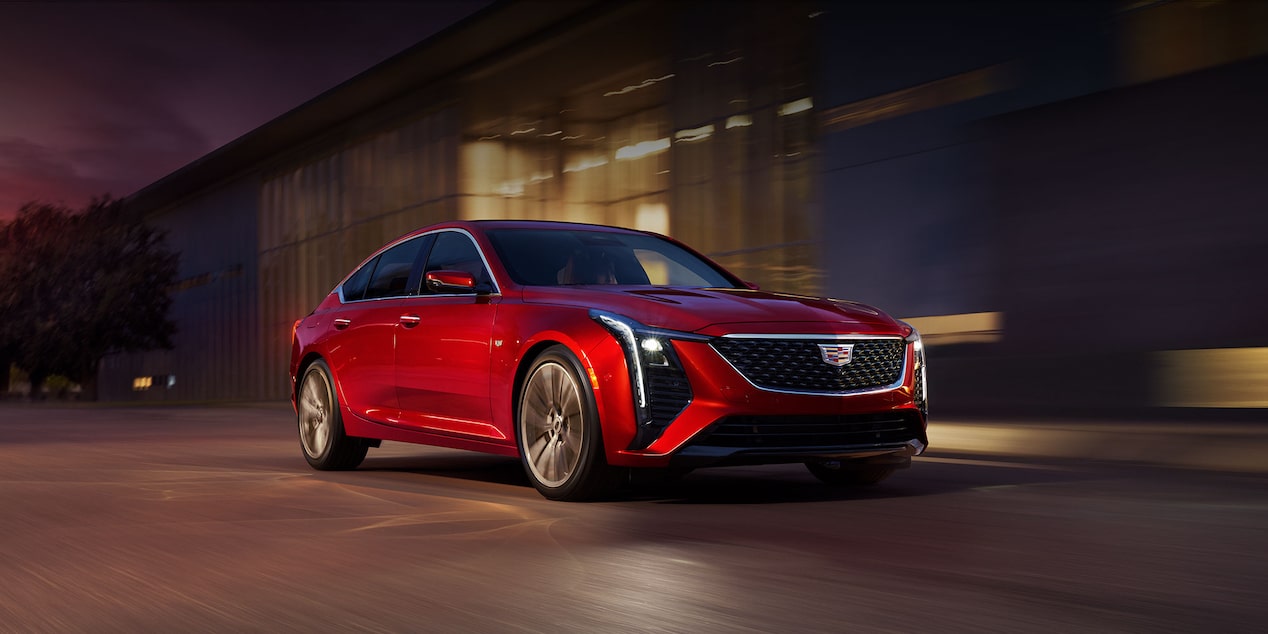 Vista delantera de medio perfil de un vehículo Cadillac CT5 2025 Rojo pasando por delante de un edificio industrial