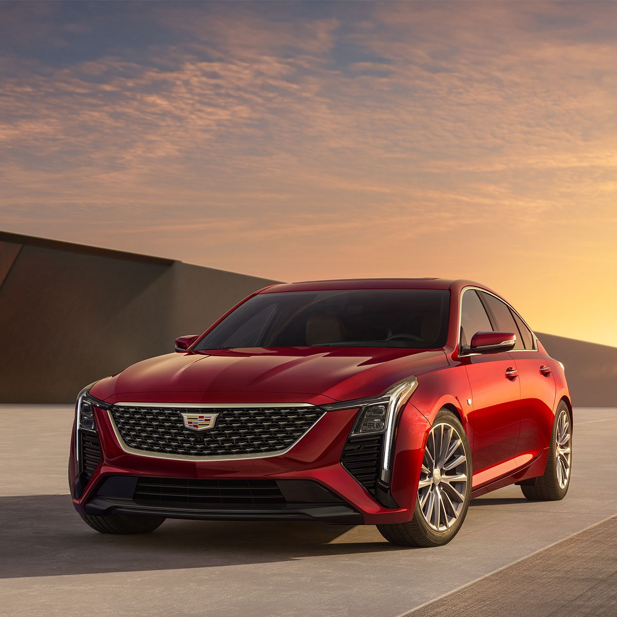 Vista lateral del lado del conductor de un Cadillac CT5 2025 rojo estacionado, con una bella puesta de sol de fondo