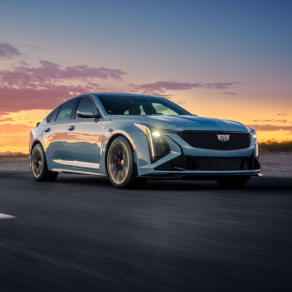 Dos Cadillac CT5 V-Series 2025 circulando por un camino sinuoso, con una asombrosa puesta de sol de fondo