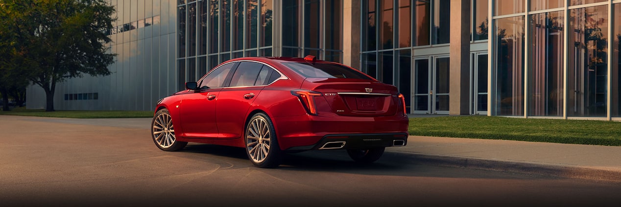 Vista trasera del vehículo Cadillac CT5 2024 en Rojo Radiante Tintcoat estacionado cerca de un edificio industrial