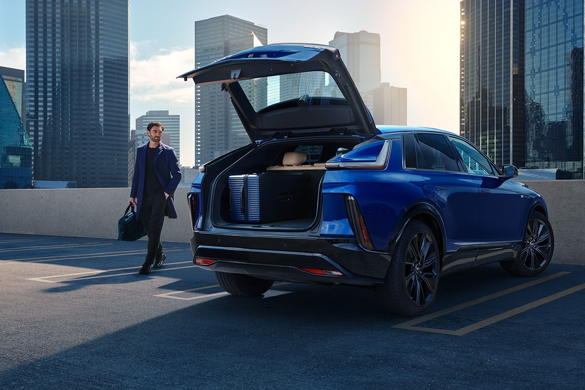 A Man Walking to an Opened Trunk of a Parked Blue 2025 Cadillac LYRIQ Outlooking the City