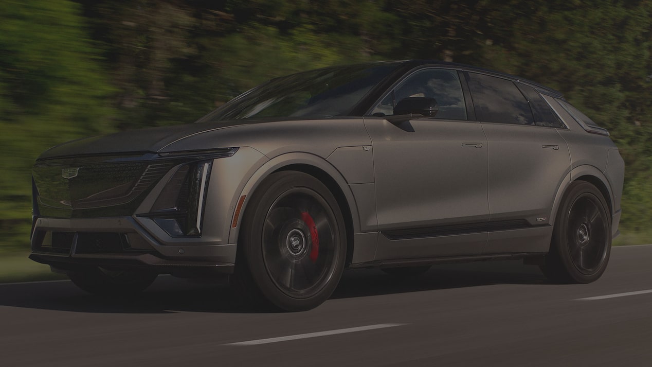 Low Three-quarter View of a Cadillac LYRIQ-V Driving Down a Road Lined with Trees