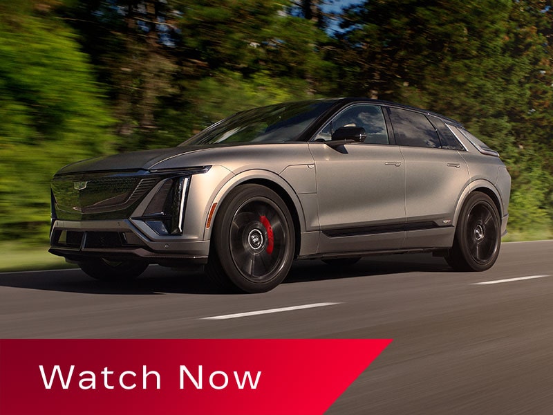 Low Three-quarter View of a Cadillac LYRIQ-V Driving Down a Road Lined with Trees