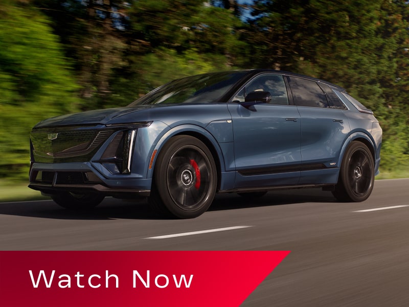 Low Three-quarter View of a Cadillac LYRIQ-V Driving Down a Road Lined with Trees