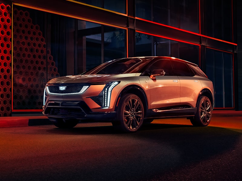 Vista de tres cuartos de una Cadillac OPTIQ 2025 estacionada con los faros delanteros encendidos