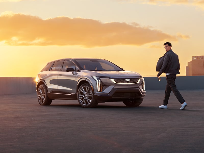 Un hombre caminando hacia una Cadillac OPTIQ 2025 durante una hermosa puesta de sol