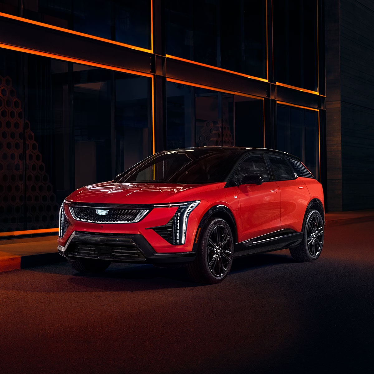 Vista en tres cuartos de una Cadillac OPTIQ 2025 roja estacionada en una calle oscura