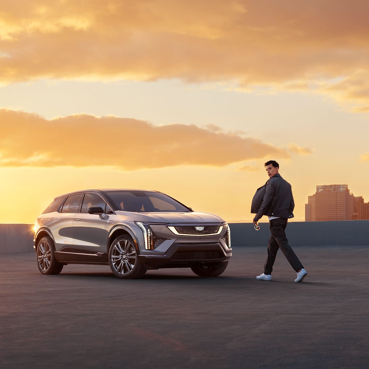 Un hombre caminando hacia una ​​​​​​​Cadillac OPTIQ 2025 durante una hermosa puesta de sol