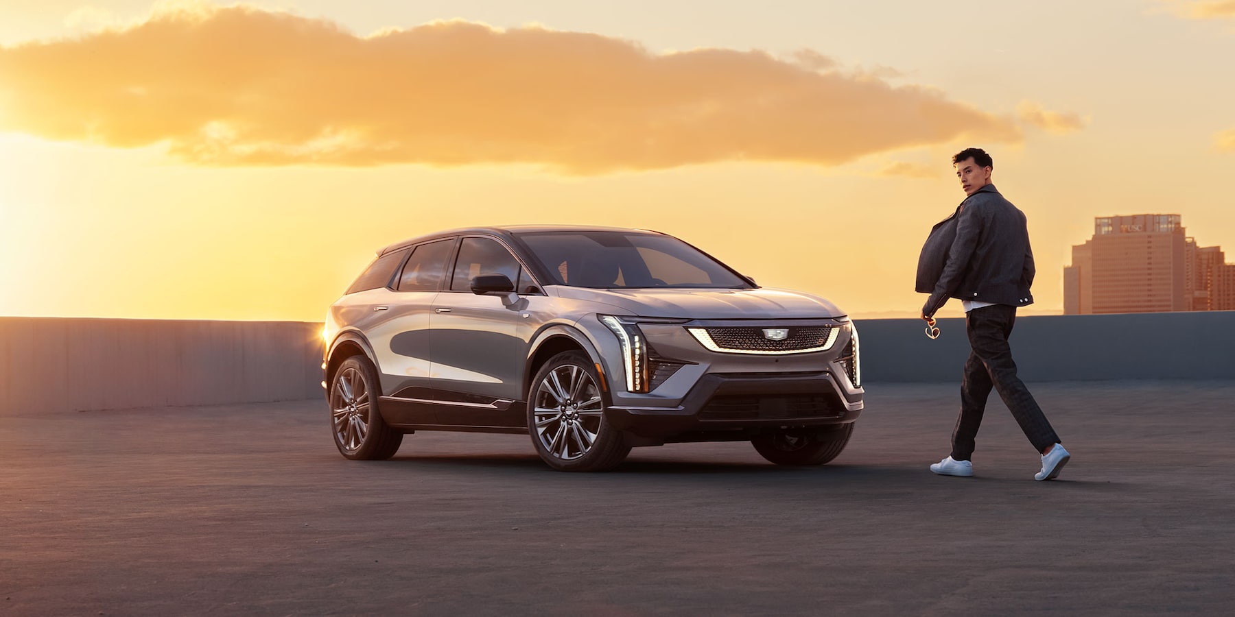 man walking to the 2025 Cadillac OPTIQ parked on a rooftop at sunset.