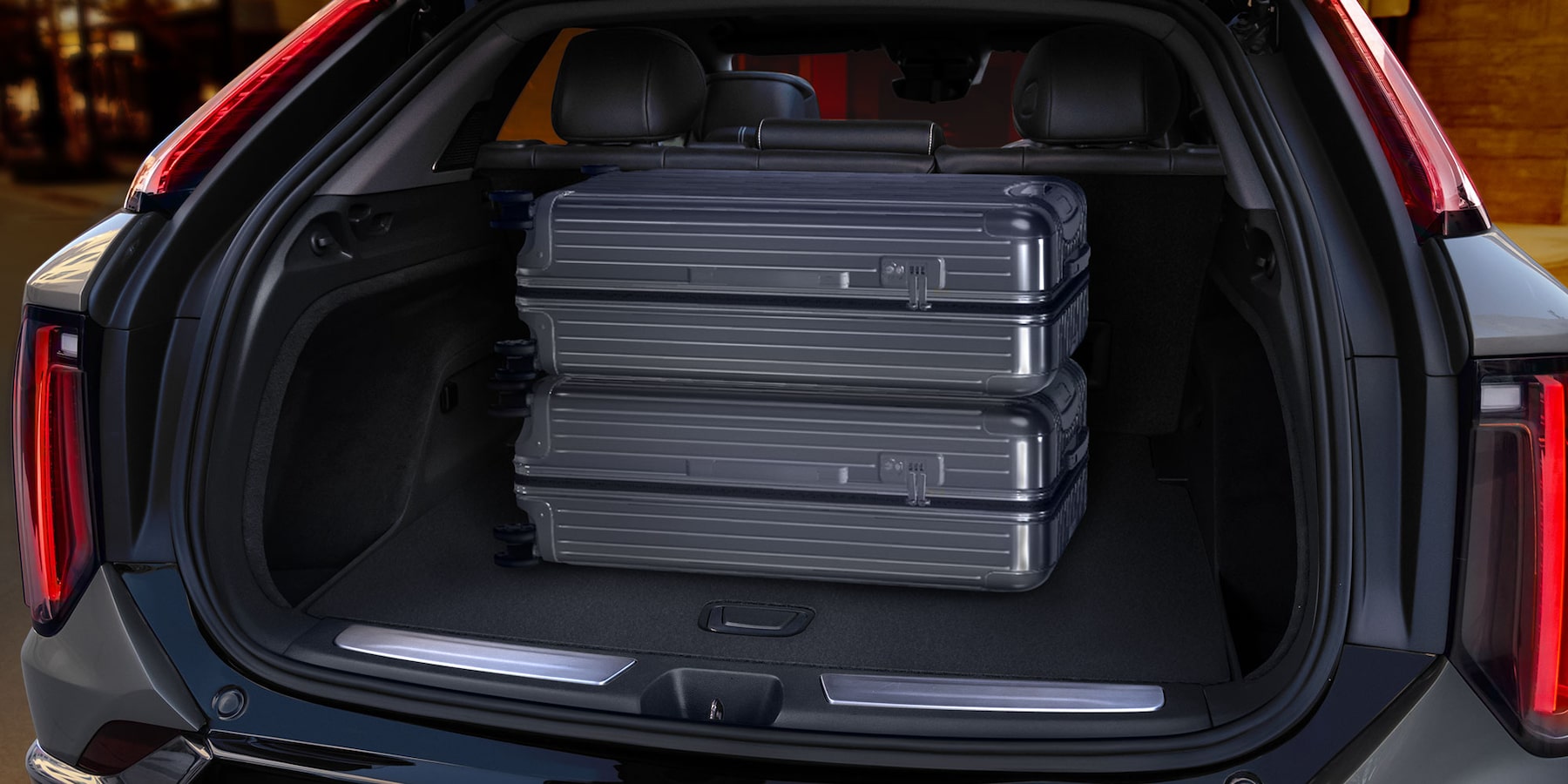 3 large luxury suitcases stacked vertically in the rear cargo trunk space of OPTIQ SUV.
