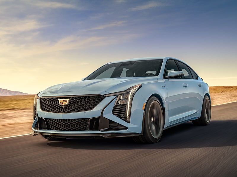 Low Three-Quarters View of a Light Blue 2025 Cadillac CT5-V Driving Down the Road Surrounded by Desert