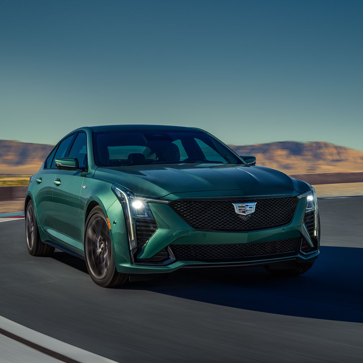 Three-Quarters View of a Green 2025 Cadillac CT5-V Driving Down the Road Surrounded by Desert