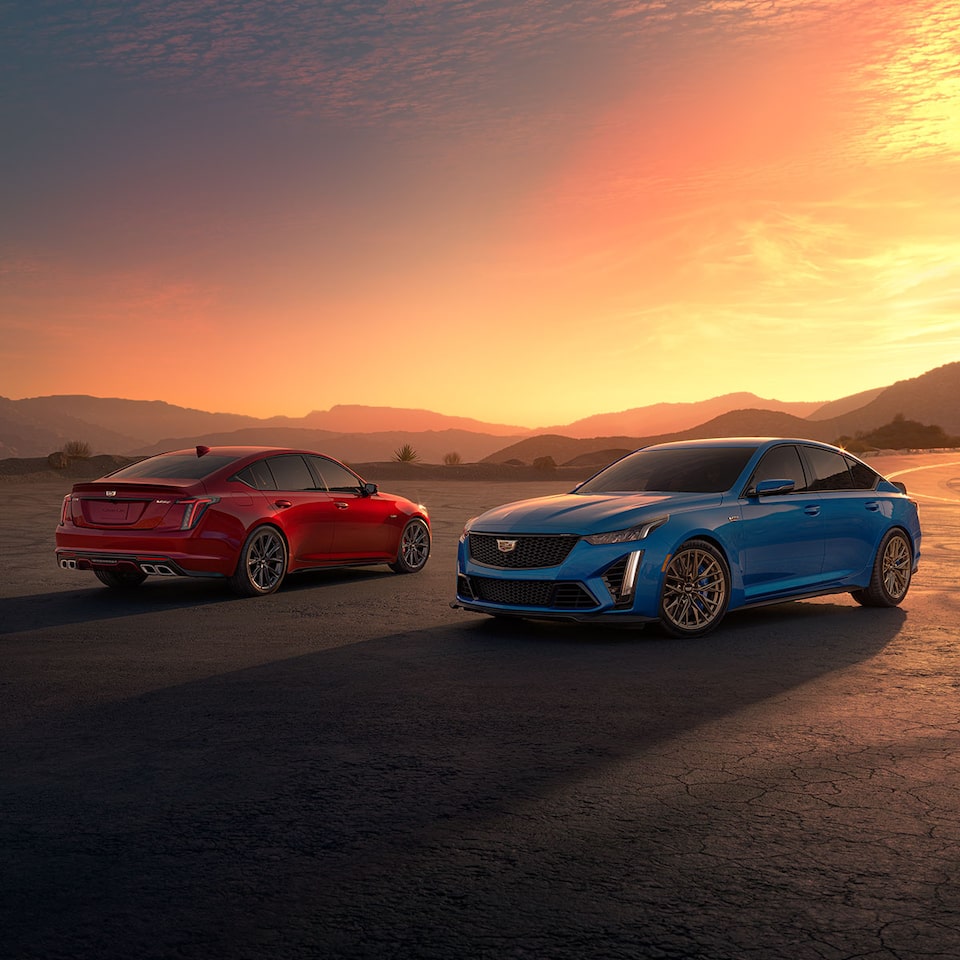 Blue and Red 2025 CTS-V's parked on the side of a desert road at sunset.